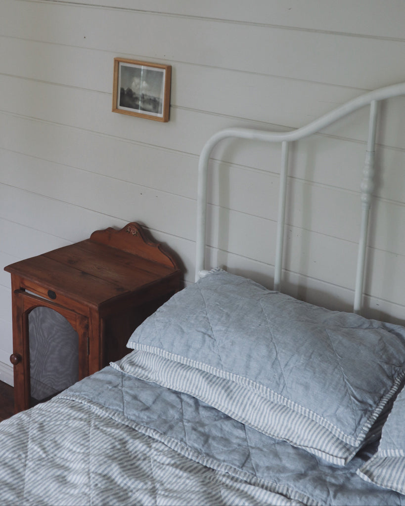 Bed with white headboard and wooden nightstand against a white paneled wall.