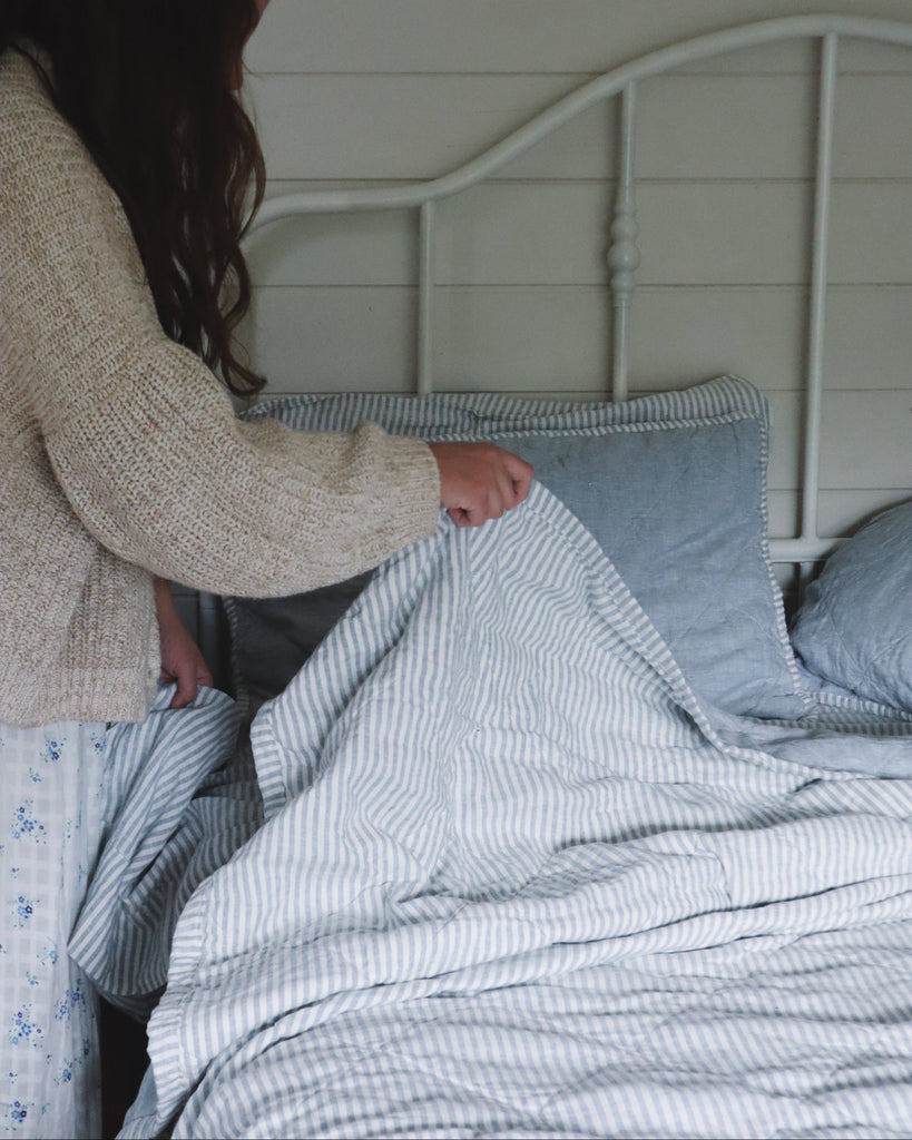Person making a bed with striped bedding in a bedroom setting