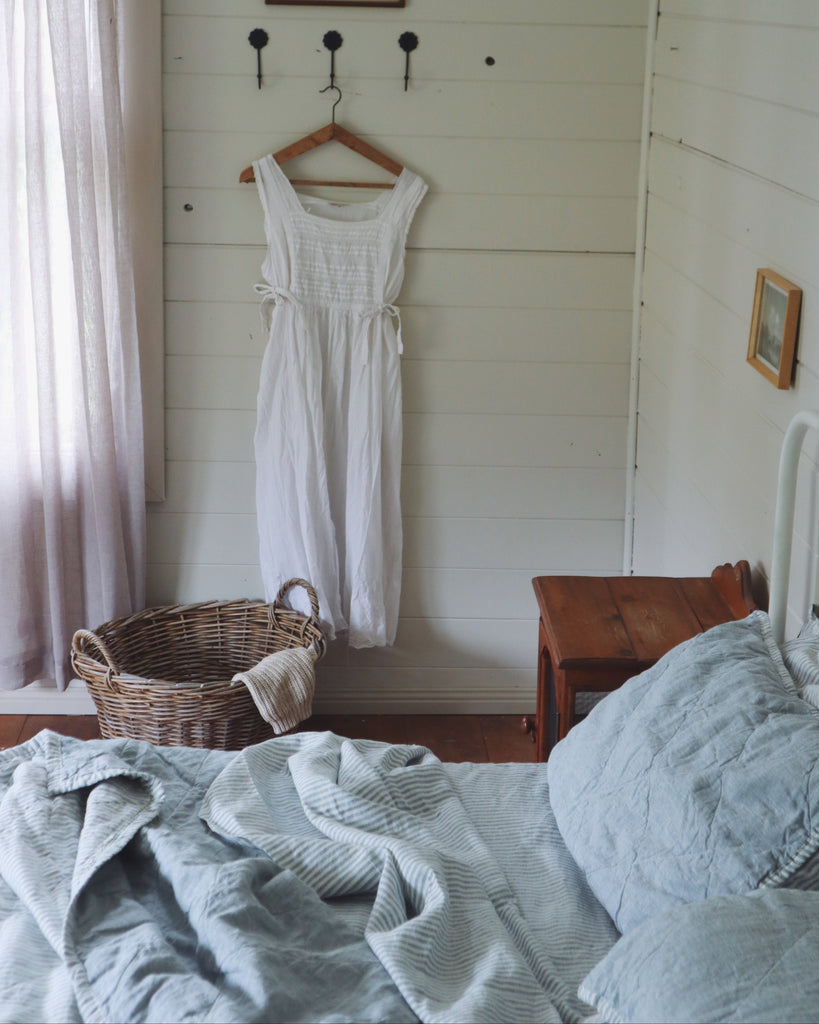 White dress hanging on a hook in a bedroom with a bed and basket.