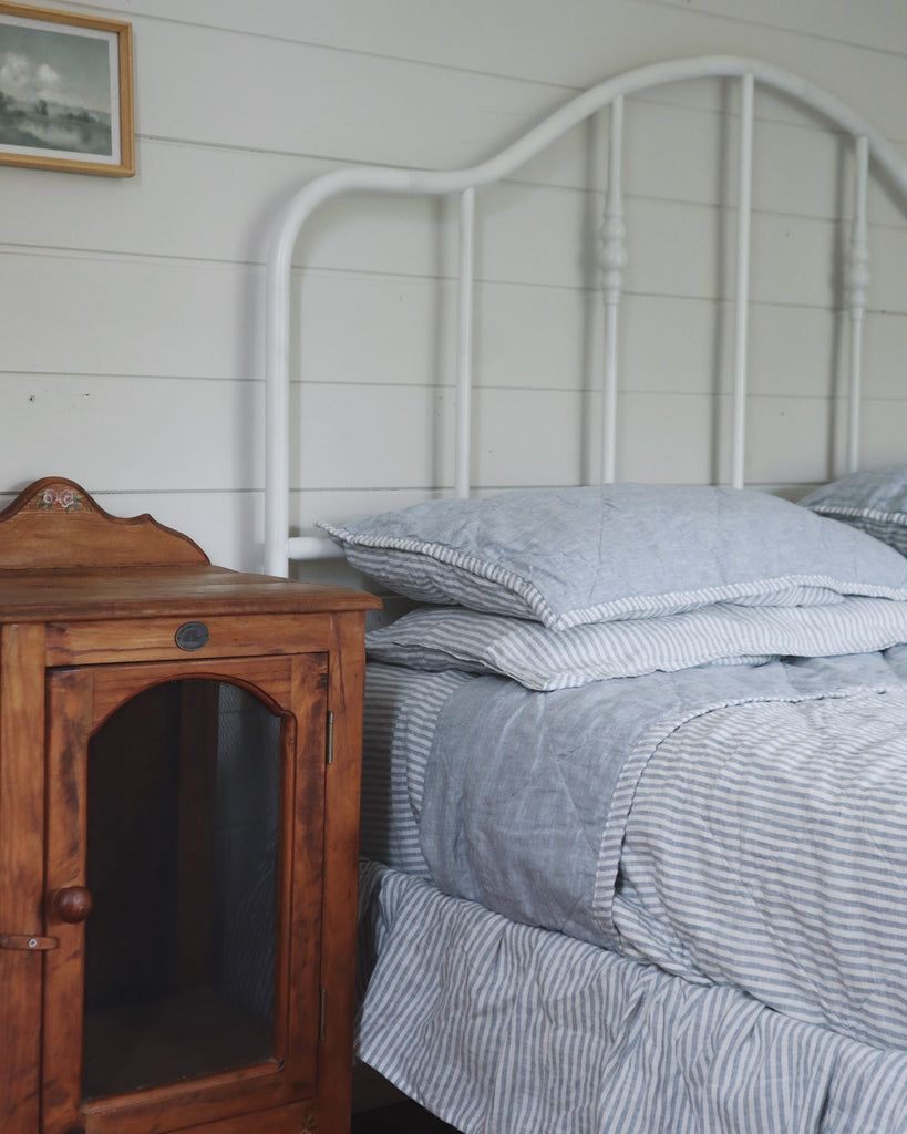 Bed with striped bedding next to a wooden nightstand against a white paneled wall.