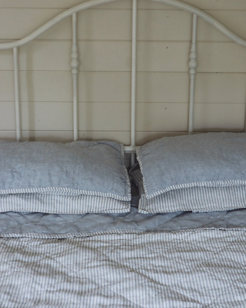 Bed with white headboard and french blue bedding against a wooden wall.