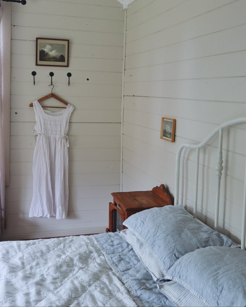 Bedroom with white walls, a bed with blue bedding, and a white dress hanging on a hook.