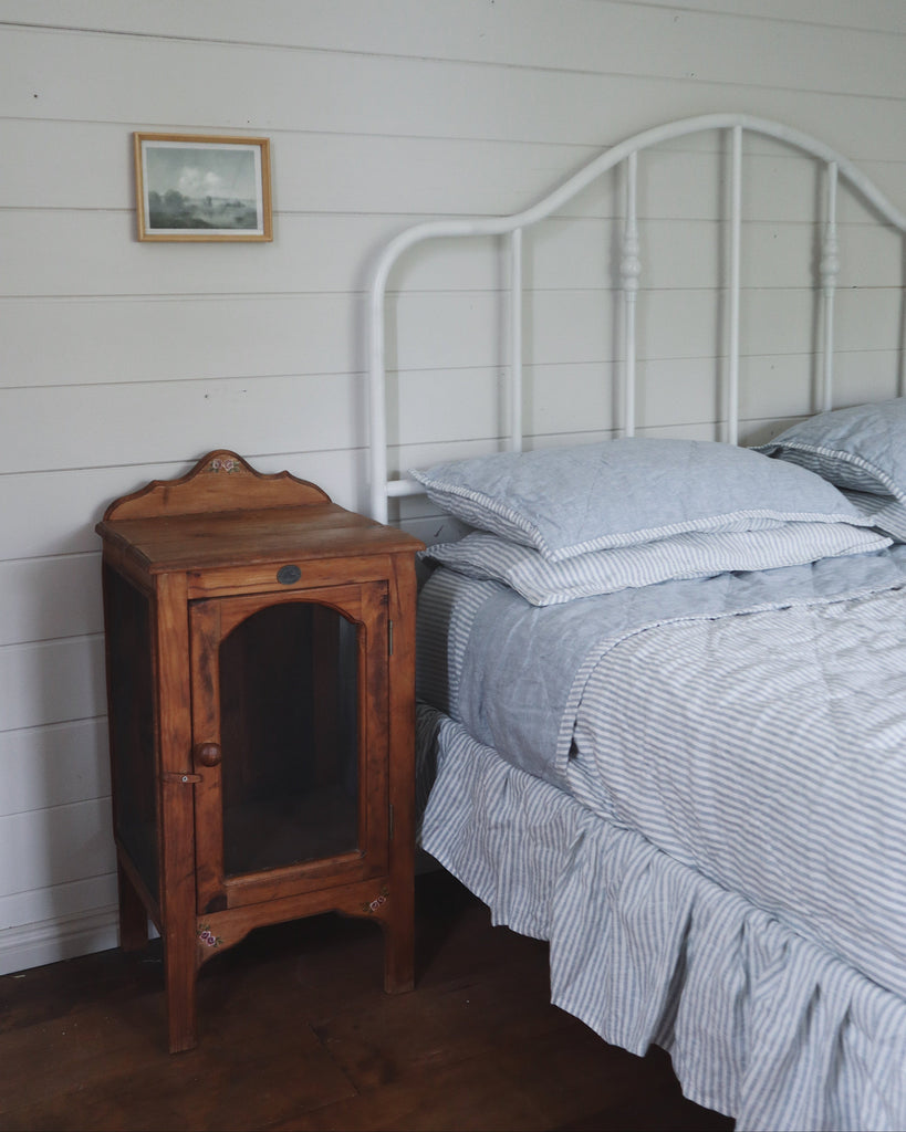 Bedroom with wooden nightstand and bed with striped bedding against a white paneled wall.