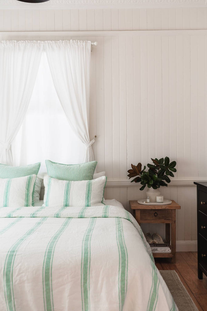 Bedroom with striped bedding and a nightstand with a plant.