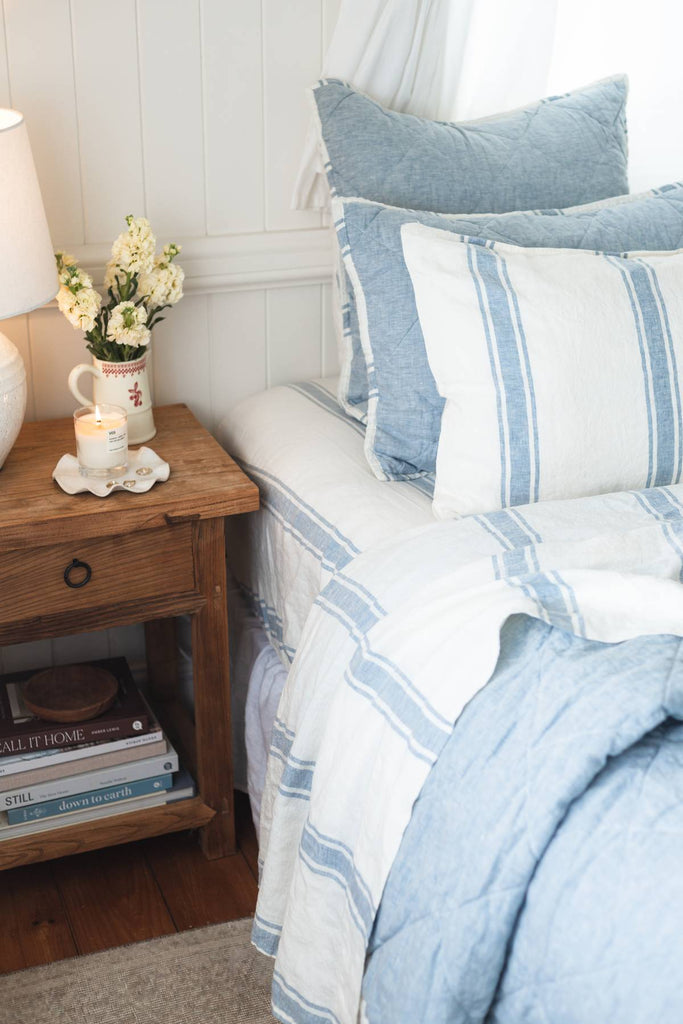 Bedroom with striped bedding, wooden nightstand, and floral arrangement.