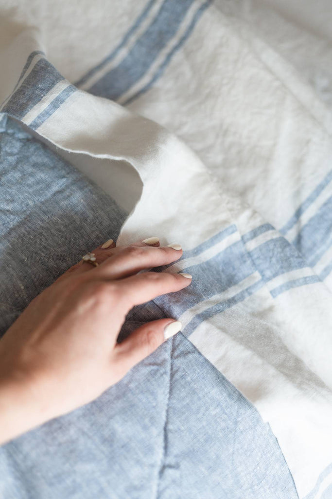Hand touching a blue and white striped fabric with a pillow in the background