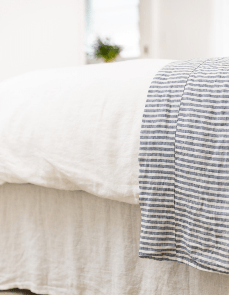 Close-up of a bed with white bedding and a striped blue and white blanket.