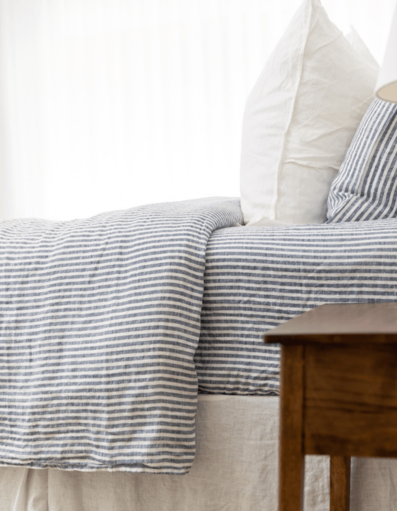 Striped bedding on a bed with a wooden nightstand in the foreground