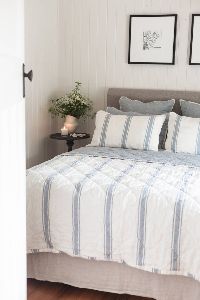 Bedroom with striped bedding, pillows, and a small table with a candle and flowers.