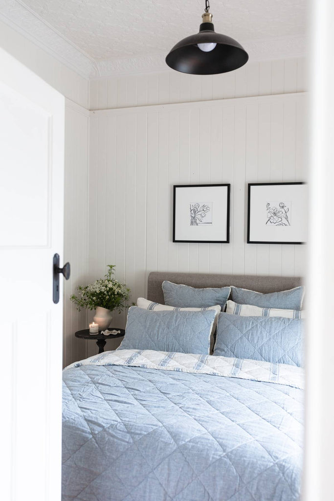 Bedroom with light blue bedding and framed artwork on the wall.