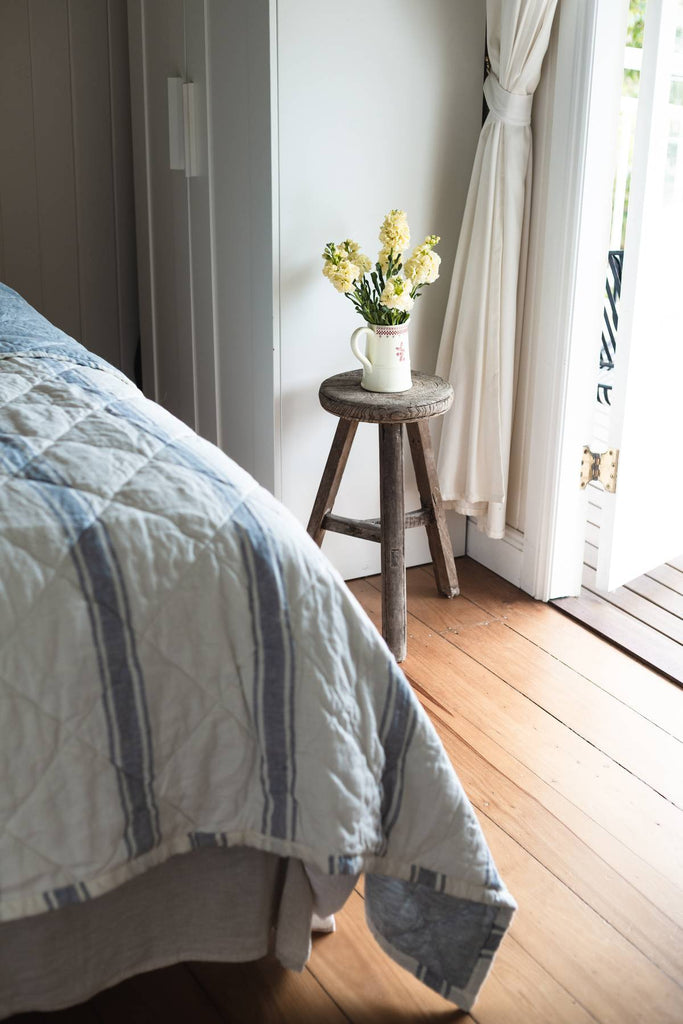 Bedroom with a wooden stool holding a vase of yellow flowers near a window.