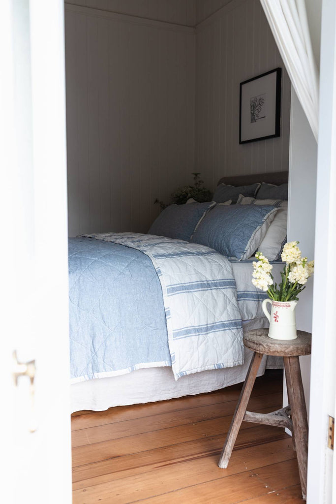 Bedroom with a bed covered in blue and white striped bedding, a small table with flowers, and a framed picture on the wall.