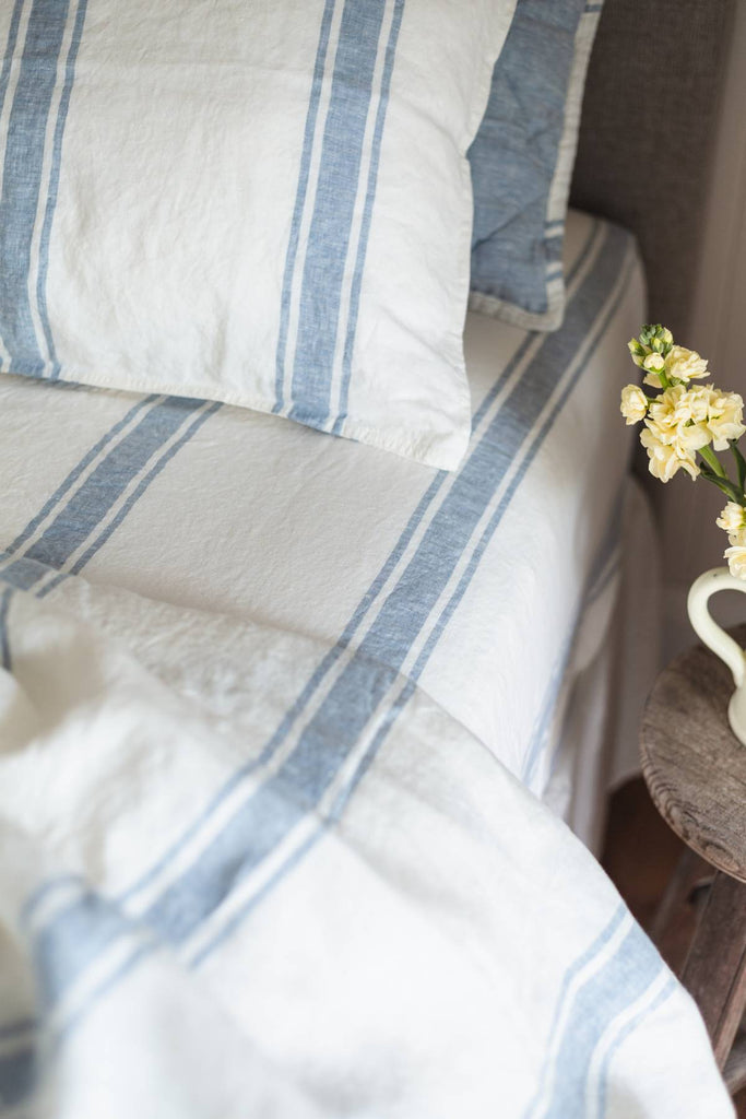 Striped bedding with blue and white lines on a bed, with a small vase of flowers on a side table.