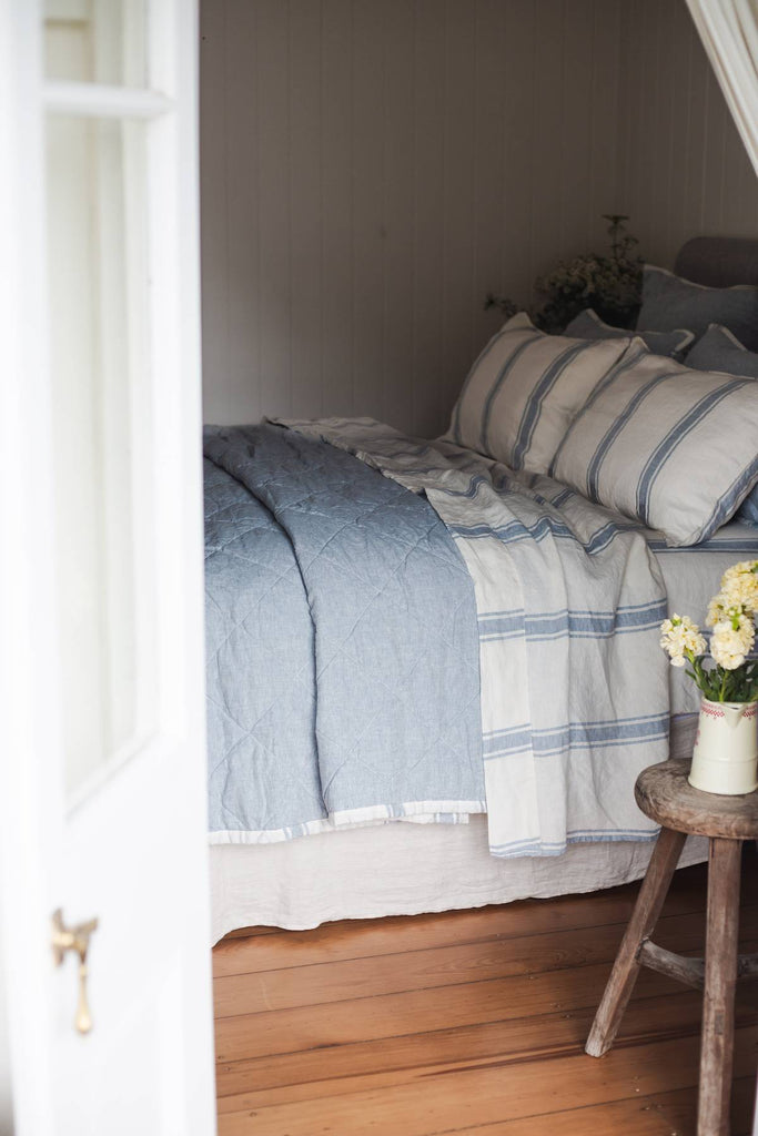 Bed with striped bedding and a wooden stool with flowers in a bedroom setting