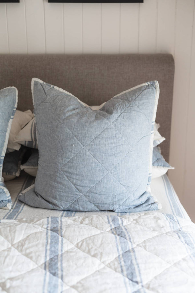 Quilted bedspread with light blue pillows on a bed against a neutral wall.
