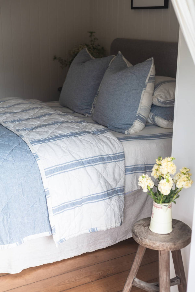 Bedroom with a bed featuring blue and white striped bedding, pillows, and a small wooden table with flowers.