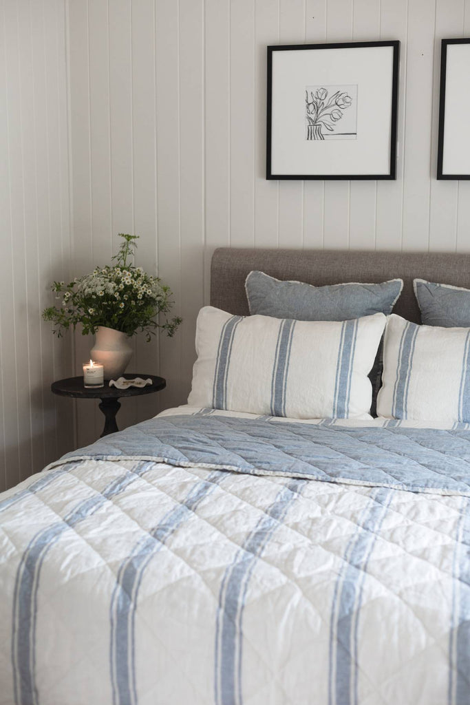 Bedroom with striped bedding, pillows, and a small table with flowers.