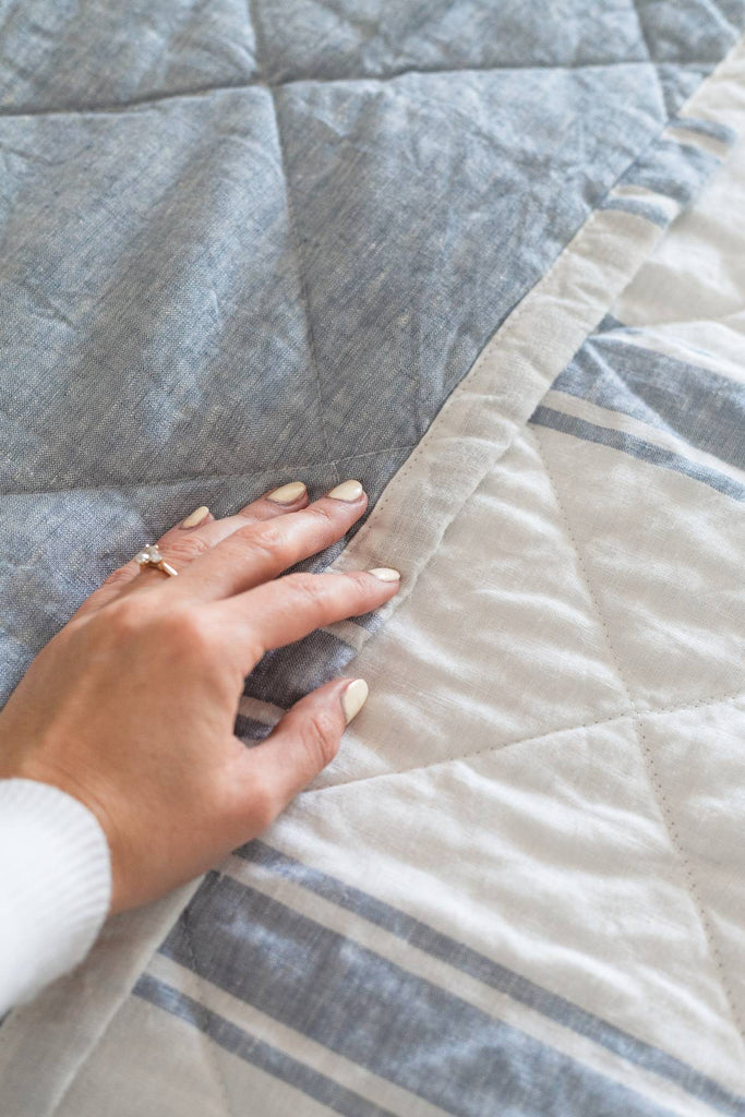 Hand touching a gray quilt with a white background